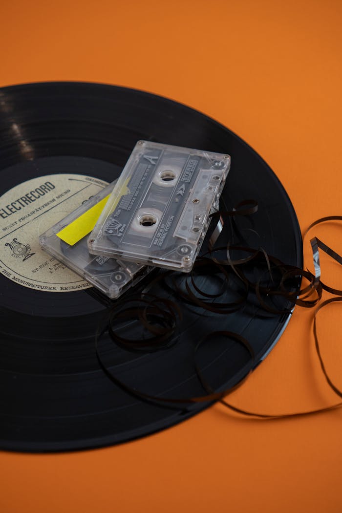 Vintage vinyl record and cassette tapes on a vibrant orange backdrop, evoking nostalgia.