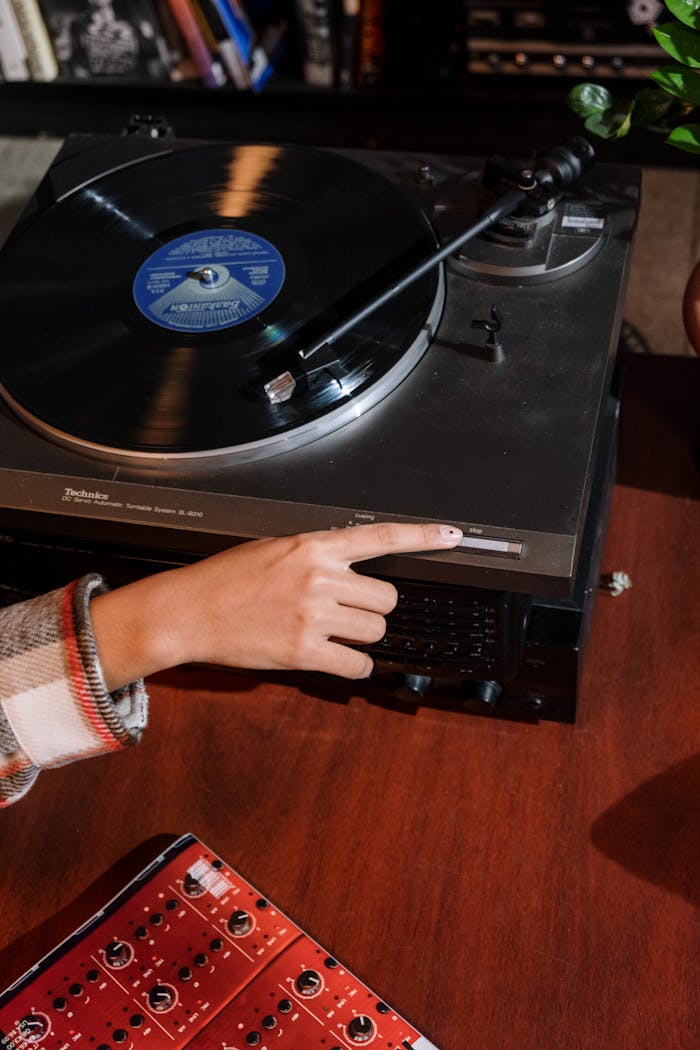 A close-up of a hand operating a vintage turntable playing a vinyl record indoors.