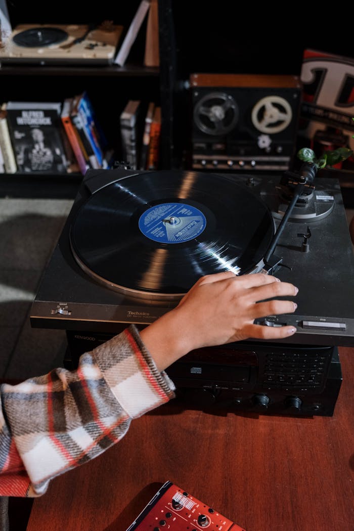 Close-up of a hand adjusting a vintage vinyl record player in a cozy room setting.